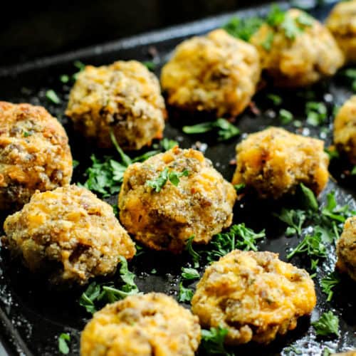low carb sausage keto balls on a black baking tray with parsley garnished over it