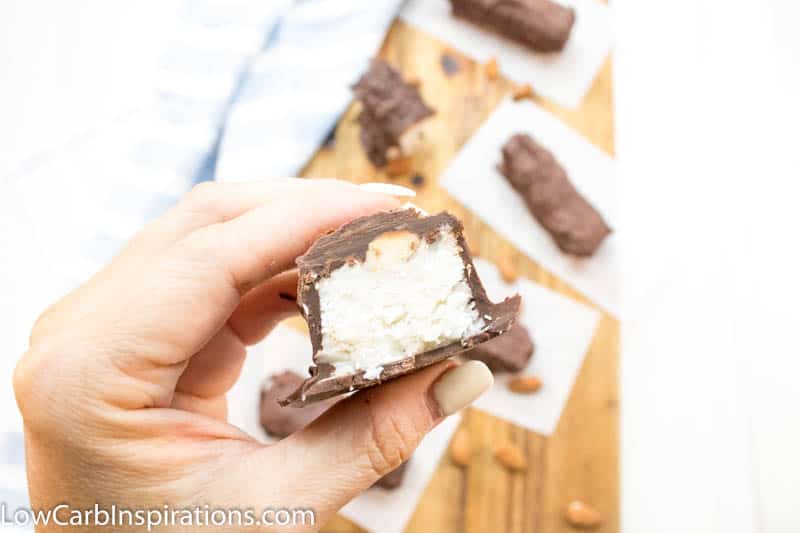 Hand holding almond joy fat bomb cut in half over top of cutting board with more bars on parchment paper