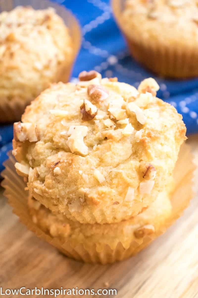 Up close picture of banana nut keto breakfast muffins stacked on a wooden cutting board with blue cloth in the background