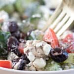 close up of greek salad with chicken in a white bowl with a gold fork