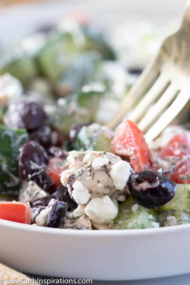 close up of greek salad with chicken in a white bowl with a gold fork