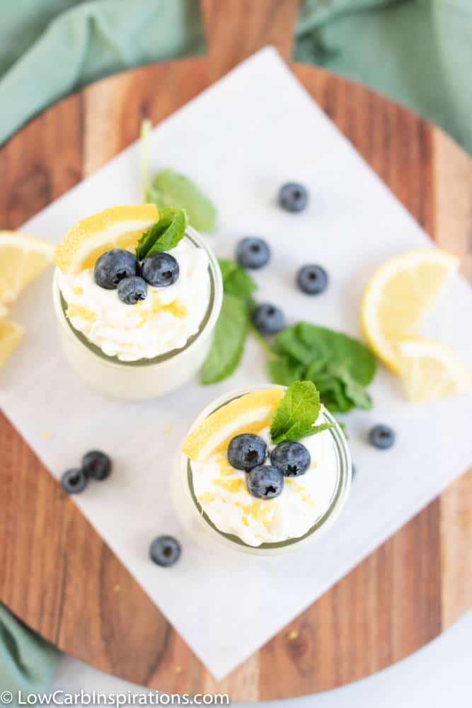 keto lemon blueberry mousse recipe in a small clear glass topped with blueberries, lemon slice and mint