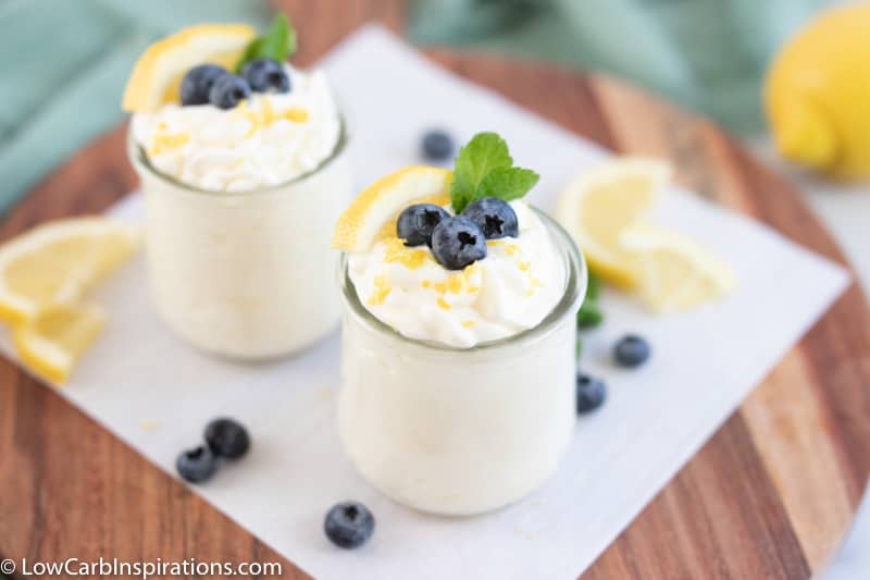 keto lemon blueberry mousse recipe in a small clear glass topped with blueberries, lemon slice and mint
