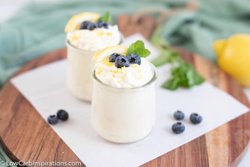 keto lemon mousse in a small clear glass with a lemon slice, blueberries and mint on a table