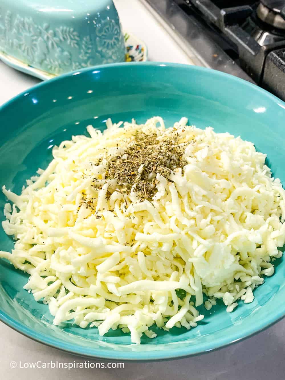 Blue bowl of shredded mozzarella cheese topped with seasonings.