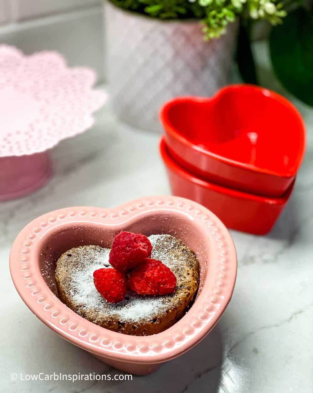 Heart shaped chocolate cake dusted with sweetener and topped with Raspberries served in a pink cake pan.