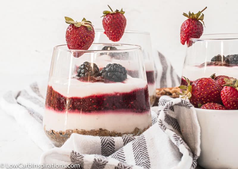 close up of berry parfait recipe on a table with strawberries next to it and more parfaits in the background