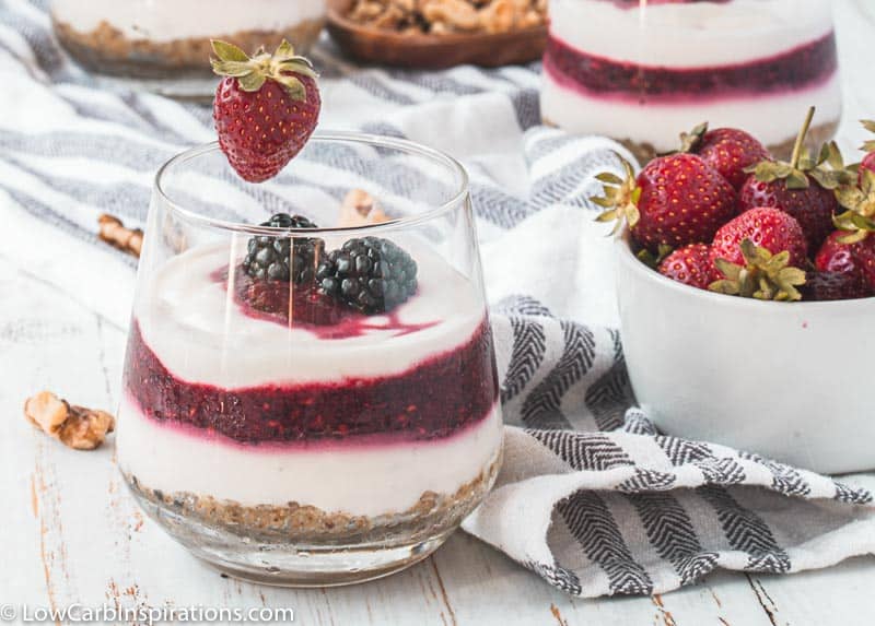 close up of berry parfait on a table with a bowl of strawberries next to it