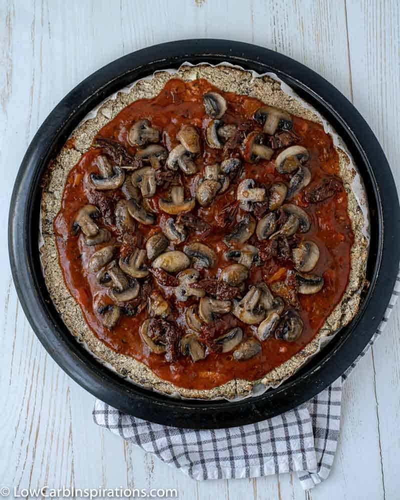 cauliflower pizza crust with sauce and cooked mushrooms on a pizza pan