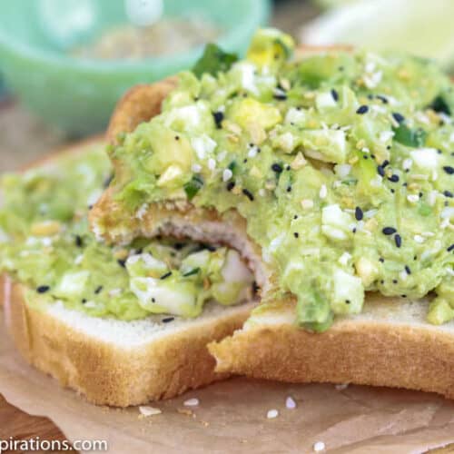 close up of avocado egg salad toast on brown parchment paper with a bite taken