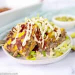 close up of easy bacon cheeseburger casserole on a white plate with pickle spears in the background