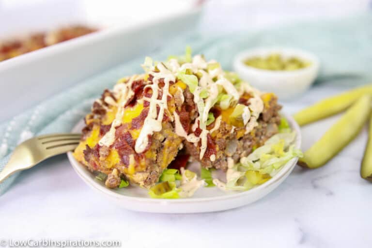 close up of easy bacon cheeseburger casserole on a white plate with pickle spears in the background