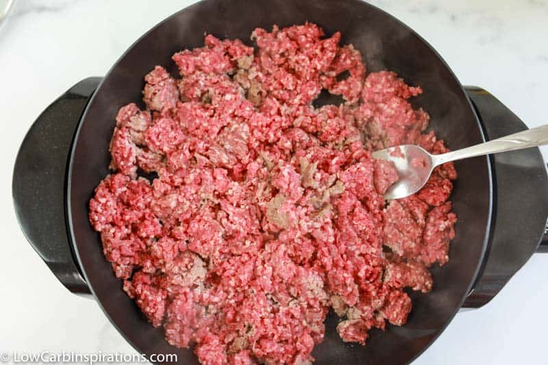 cooking ground beef in a cast iron skillet with a spoon in the skillet