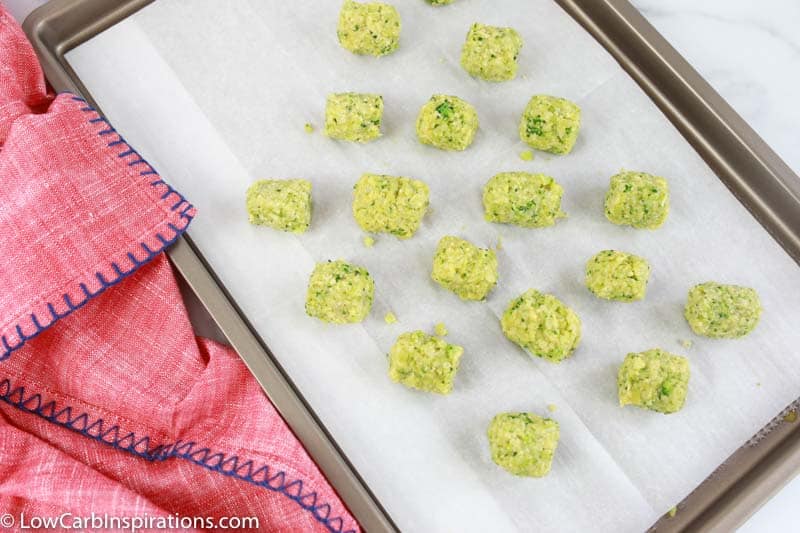 low carb broccoli tots on parchment paper and baking sheet with a pink towel on the side 