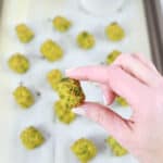 baked broccoli tots on parchment paper and baking sheet with a handing holding one close up