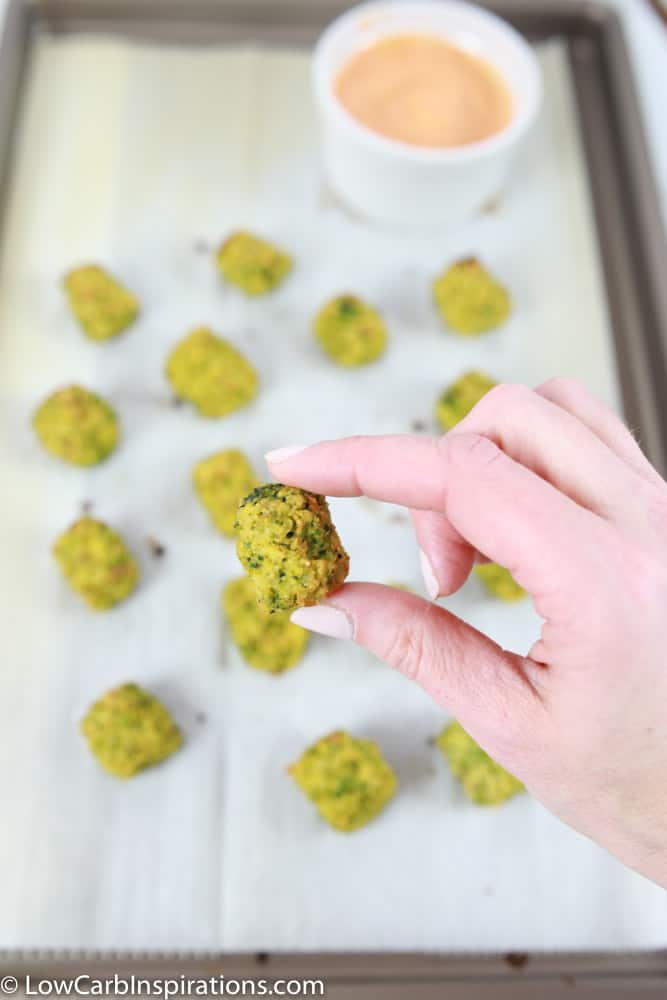 baked broccoli tots on parchment paper and baking sheet with a handing holding one close up