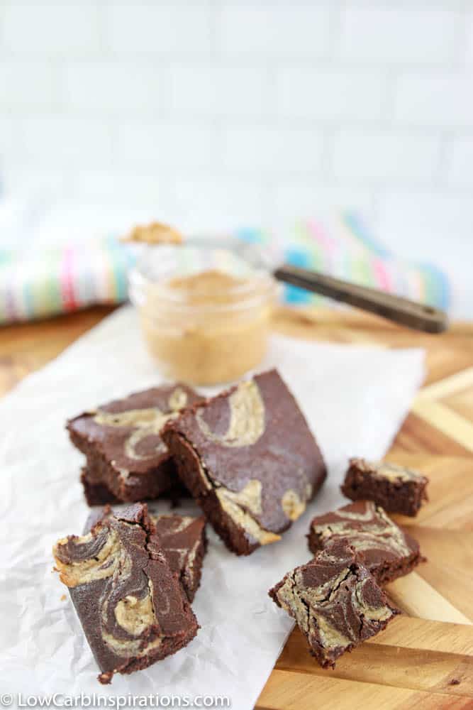 peanut butter swirl brownies cut into squares on a wood cutting board with peanut butter in a bowl in the background