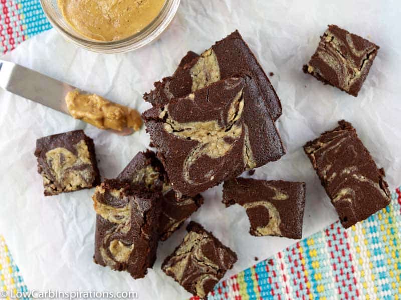 overhead photo of chocolate peanut butter brownies on a wood cutting board with peanut butter in a glass bowl in the background