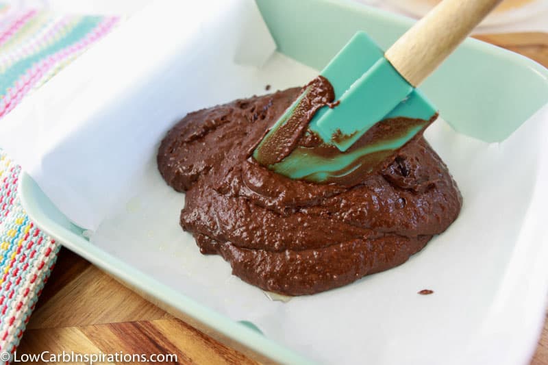 adding keto brownie recipe ingredients in a 9x9 baking dish with a baking spatula