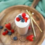 overhead photo of the finished protein shake recipe in a clear class on a wood board with berries and straws on the side