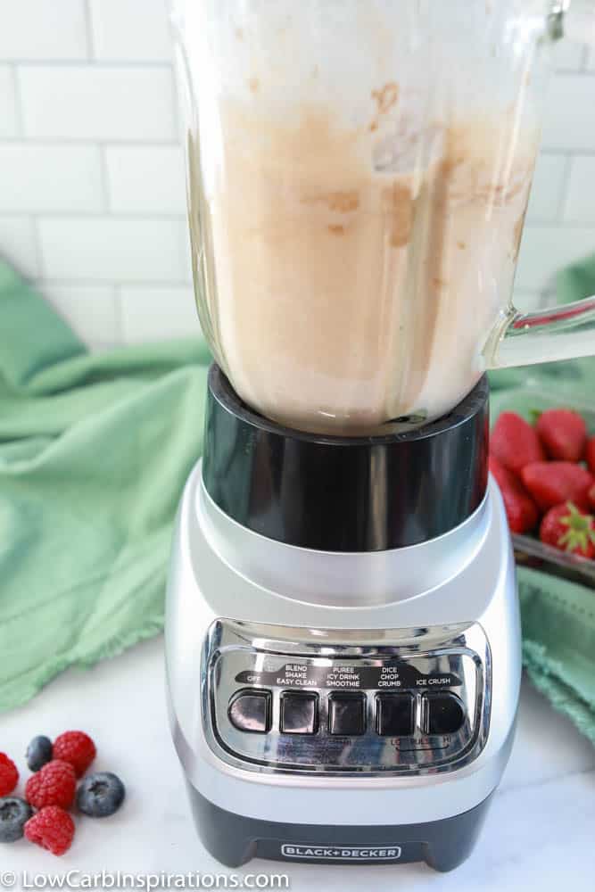keto protein shake ingredients in a blender on the counter with strawberries in the background