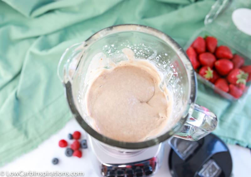 keto protein shake ingredients blended together in a blender on the counter with strawberries in the background