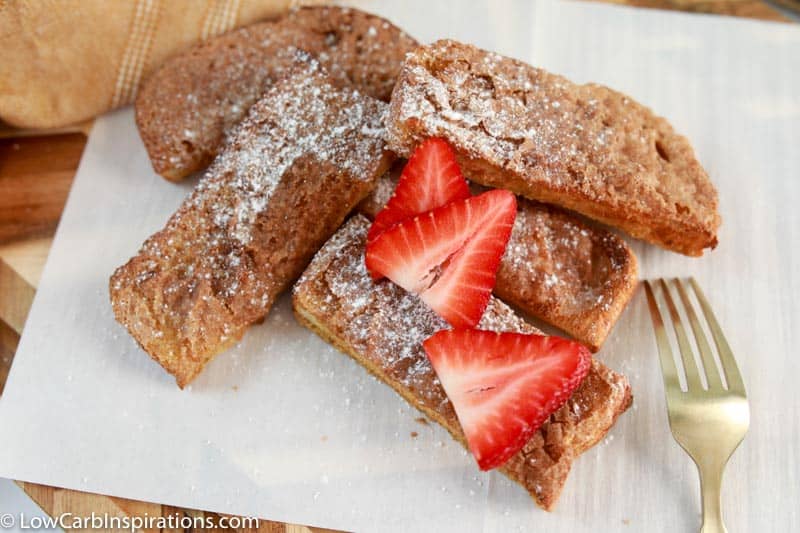 finished air fryer french toast sticks on parchment paper with strawberries on top