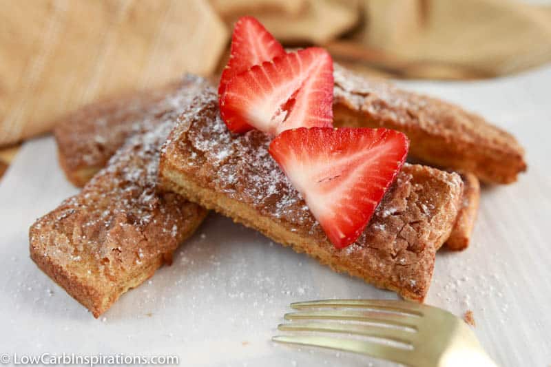close up of air fryer french toast sticks on parchment paper with strawberries on top