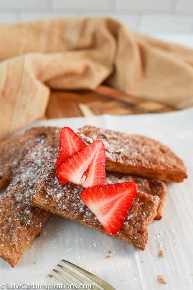 close up of air fryer french toast sticks on parchment paper with strawberries on top