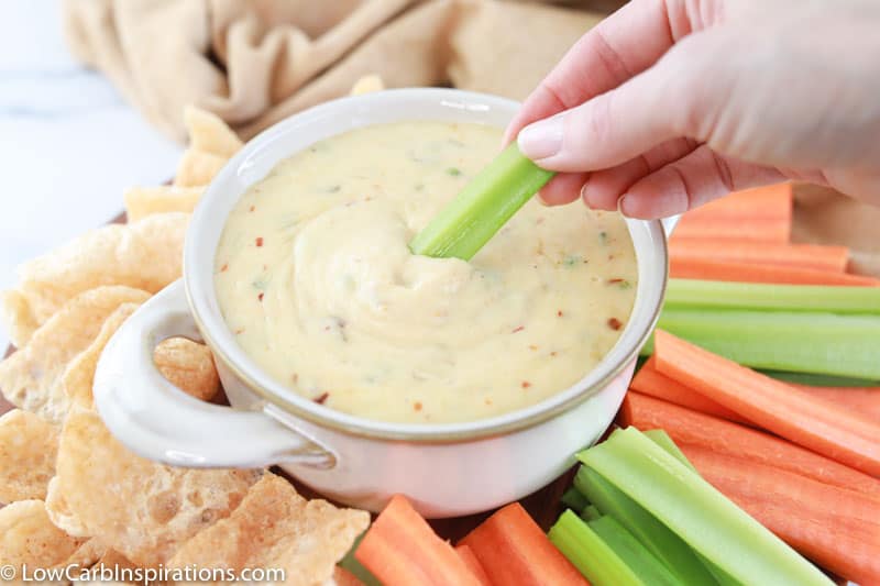 dipping celery sticks in the white cheese sauce with more celery, carrots and pork rinds around the edges