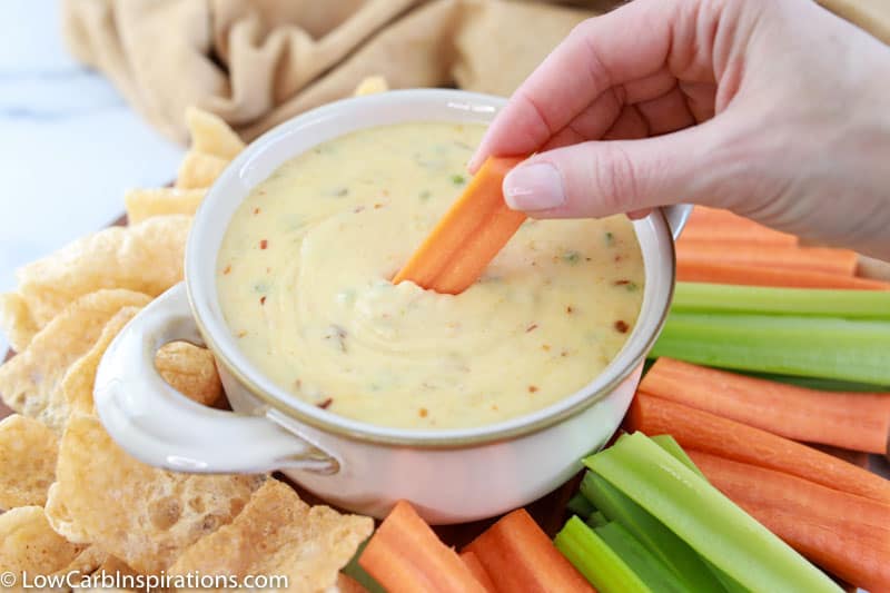 dipping carrot sticks in the white cheese sauce with more celery, carrots and pork rinds around the edges