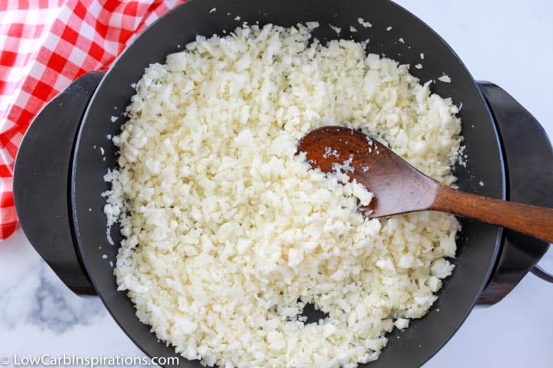 cooking cauliflower rice in a wok with a wooden spoon