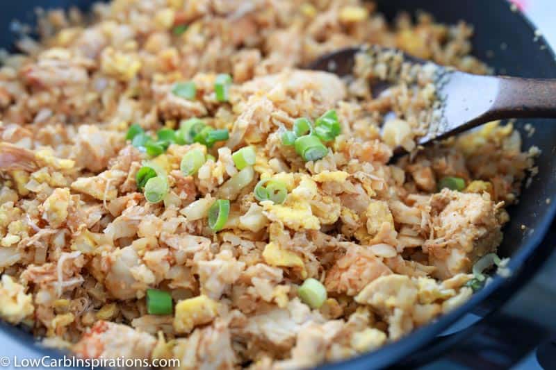 close up of keto fried rice in a wok with a wooden spoon in the pan