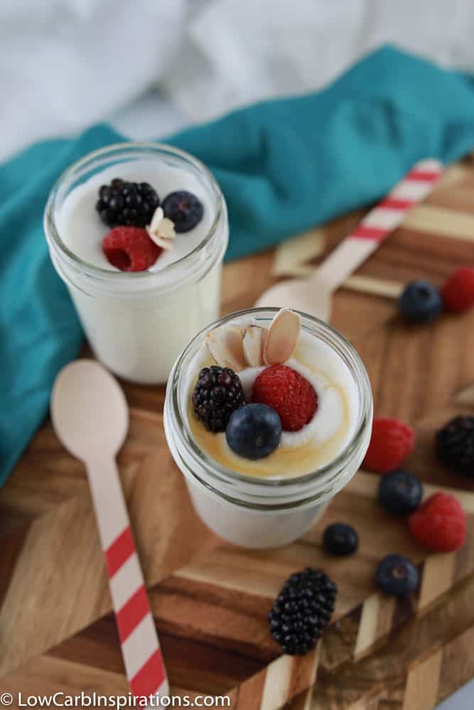 overhead photo of sugar free yogurt on a wooden board with wooden spoons and mixed berries on the side