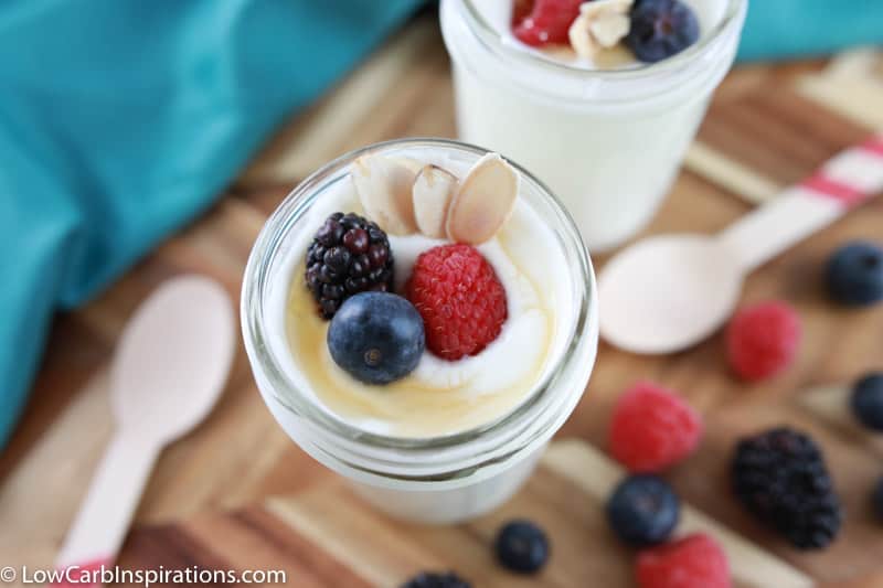 close up photo of sugar free yogurt on a wooden board with wooden spoons and mixed berries on the side