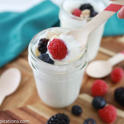 close up photo of easy yogurt recipe on a wood board with mixed berries and a wooden spoons on the side and spoonful on a spoon with a raspberry