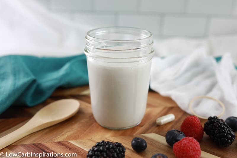 coconut yogurt recipe ingredients with mixed berries and a wooden spoon on a cutting board with cheesecloth and towel in the background