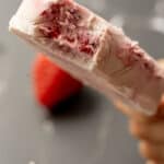 close up of homemade berry popsicles with a bite taken out with strawberries in the background