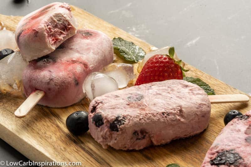 close up of triple berry popsicles on a wooden board with strawberries and berries on the side