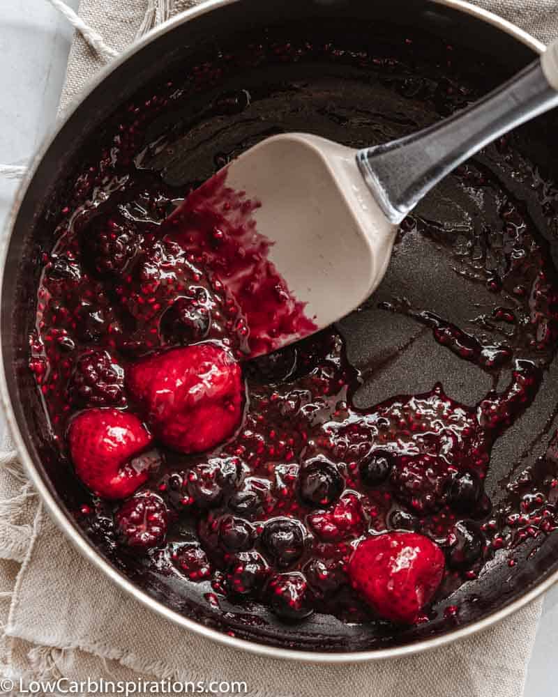 mixed berries in a sauce pan mixed together with a spatula in the pan