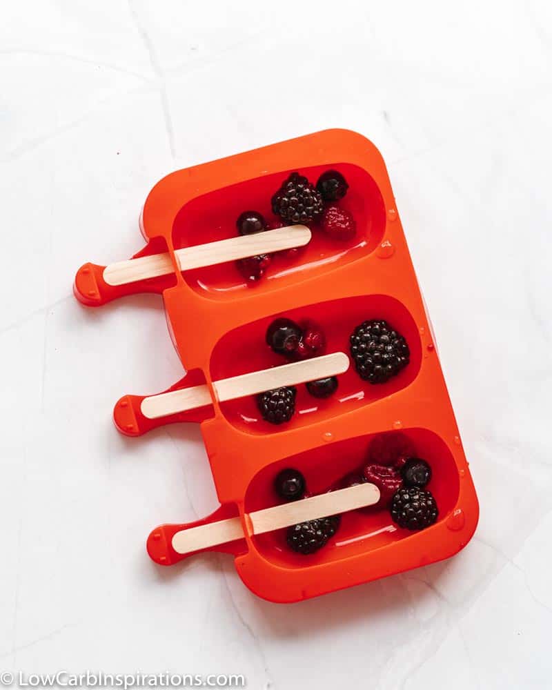 mixed berries in a popsicle mold with wooden popsicle sticks