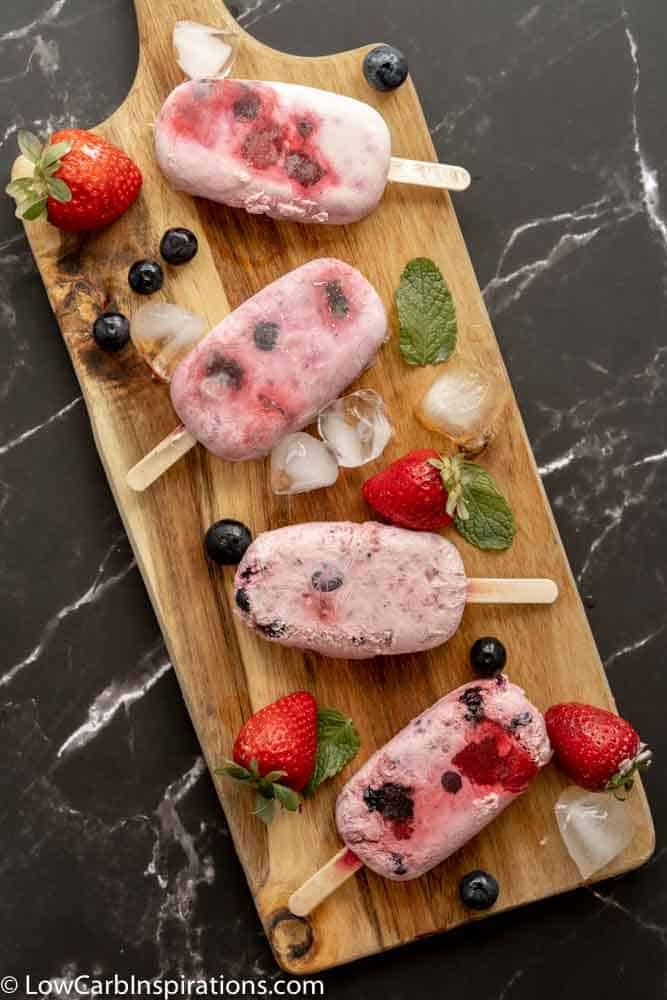 overhead photo of easy homemade popsicles on a wooden board with berries and ice on the side