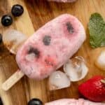 overhead photo of easy homemade popsicles on a wooden board with berries and ice on the side