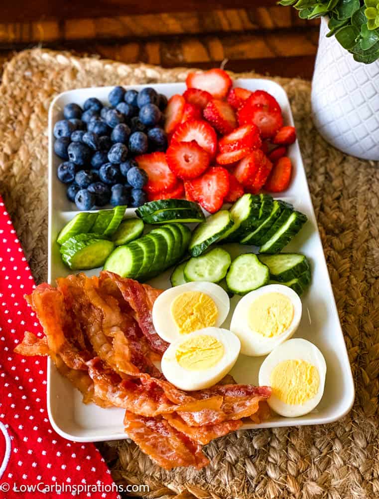 Keto friendly breakfast with blueberries, strawberries, cucumbers, eggs, and bacon on a plate