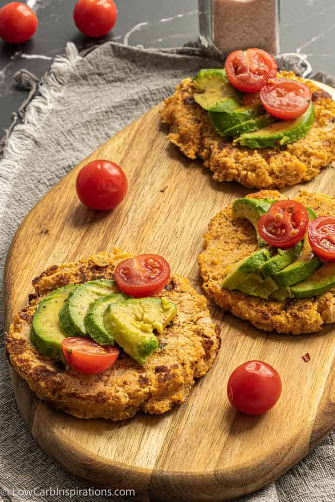 savory pancakes on a wood cutting board topped with avocado and tomatoes
