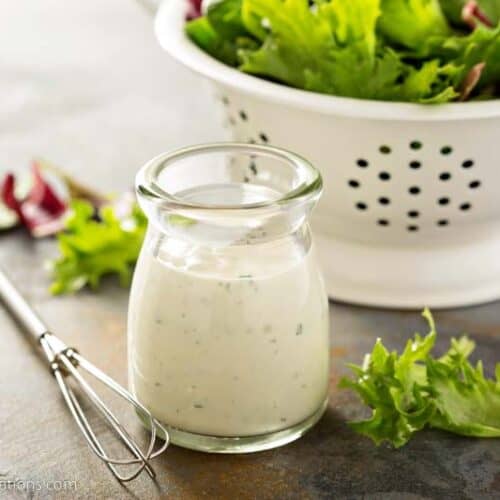 Homemade ranch dressing in a small jar with fresh greens