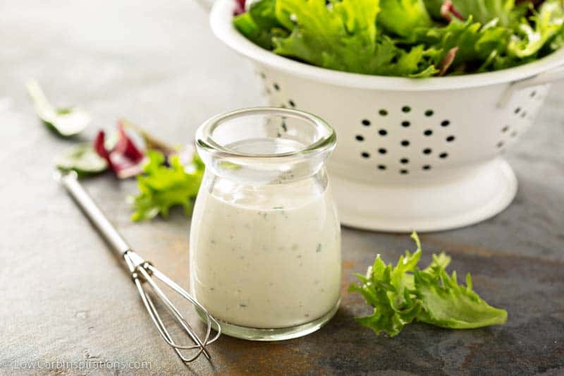 Homemade ranch dressing in a small jar with fresh greens