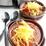 overhead shot of chili topped with cheese in a bowl in front of the crockpot