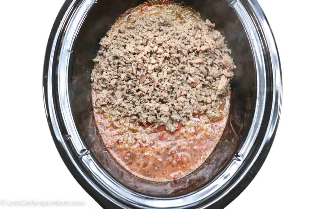keto chili ingredients in a slow cooker bowl topped with cooked ground beef and sausage